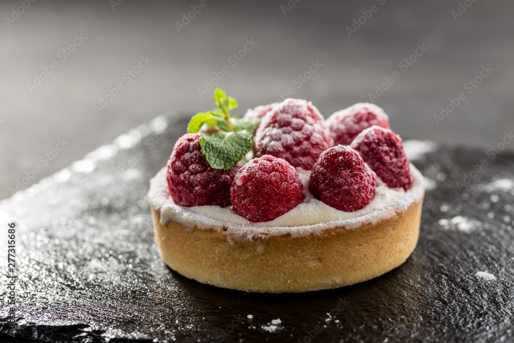 Raspberry tartlets with icing sugar close up on stone board on black background - obrazy, fototapety, plakaty 