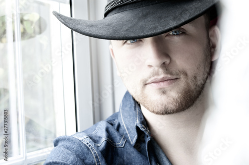 Portrait of handsome cowboy wearing hat sitting in window
