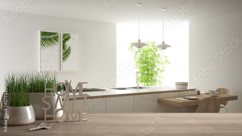 Wooden table  desk or shelf with potted grass plant  house keys and 3D letters making the words home sweet home  over modern white kitchen  interior design  blur background