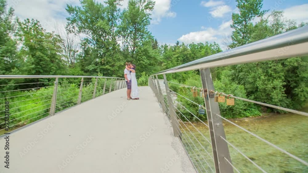 A young couple is kissing in the middle of a bridge. It's summer time. A young couple is kissing in the middle of a bridge. It's summer time.