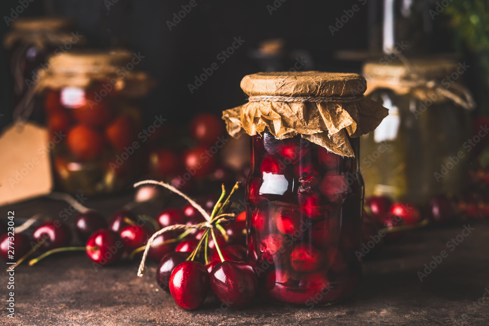 Cherry fruit compote in glass jars on dark rustic kitchen table. Close up. Preserved organic food from garden. Canning and conservation of harvest. Healthy homemade food - obrazy, fototapety, plakaty 
