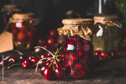 Cherry fruit compote in glass jars on dark rustic kitchen table. Close up. Preserved organic food from garden. Canning and conservation of harvest. Healthy homemade food