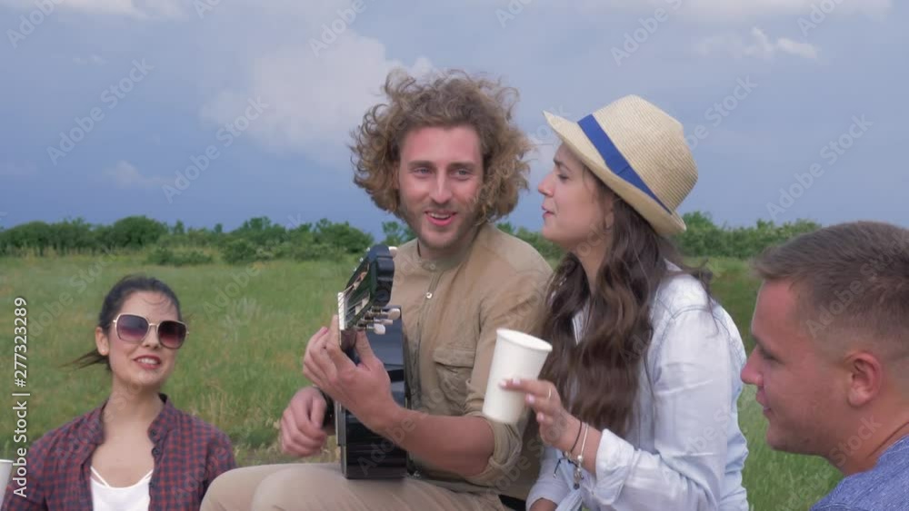 party outdoors, cheerful youth company of boys and girls play stringed musical instrument and sing while relaxing in green nature party outdoors, cheerful youth company of boys and girls play stringed musical instrument and sing while relaxing in green nature