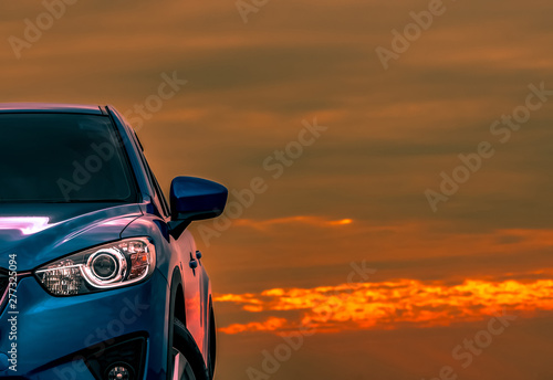 Front view of blue compact SUV car with sport and modern design parked on concrete road at sunset with beautiful orange sky. Electric car technology. Automotive industry. Car care business background. © Artinun