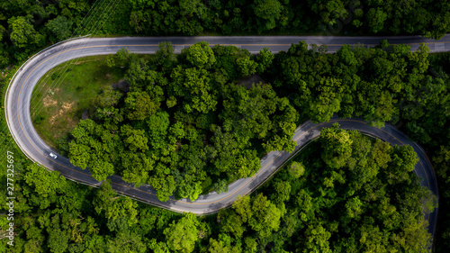 Fototapeta Naklejka Na Ścianę i Meble -  Aerial view over tropical tree forest with a road going through with car, Forest Road.