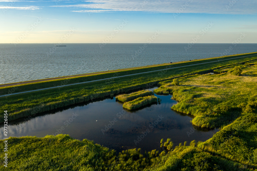 A dike in The Netherlands protecting water from flooding the land. A small natural lake in the foreground A dike in The Netherlands protecting water from flooding the land. A small natural lake in the foreground