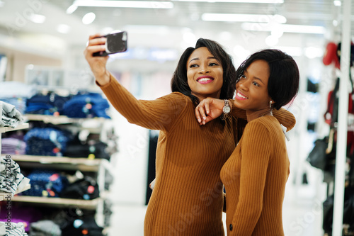 Two models african american woman in brown tunic dress posed at boutique clothes store and making selfie on phone. It s time for shopping.