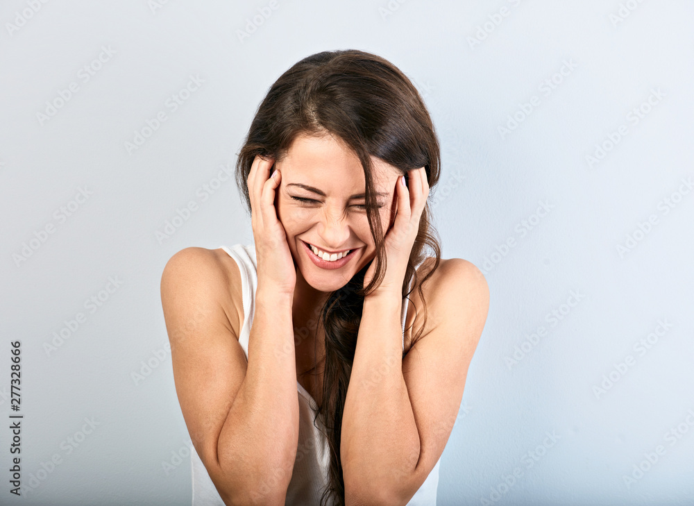 Beautiful natural toothy laughing woman with closed eyes holding the head in white shirt with long curly hairstyle. Closeup portrait Beautiful natural toothy laughing woman with closed eyes holding the head in white shirt with long curly hairstyle. Closeup portrait