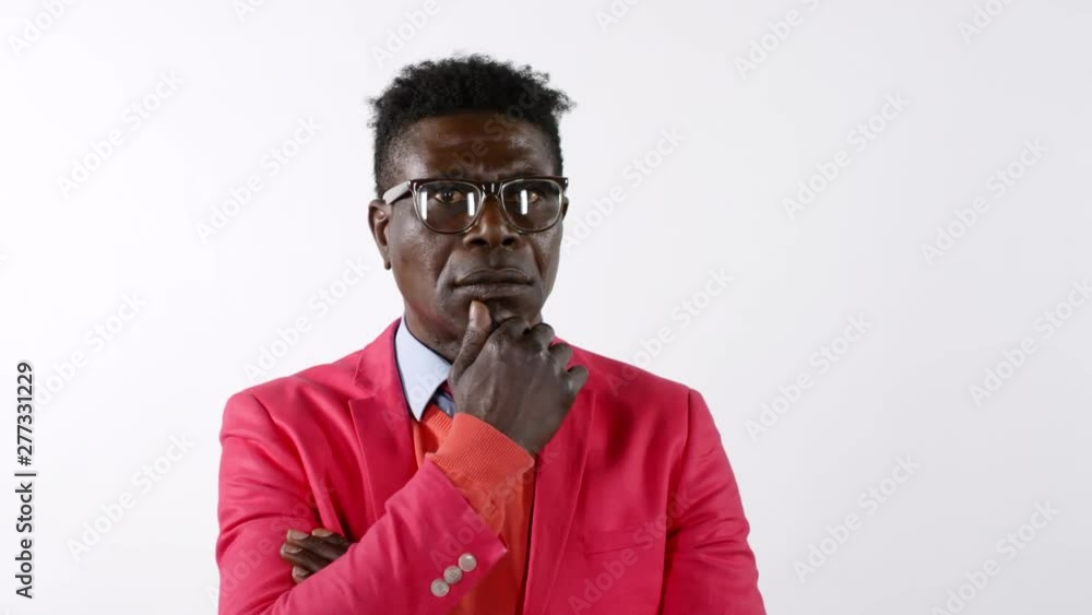 Portrait of fashionable middle aged African man in bright red suit and eyeglasses holding hand on chin and looking at camera thoughtfully while posing against white background Portrait of fashionable middle aged African man in bright red suit and eyeglasses holding hand on chin and looking at camera thoughtfully while posing against white background
