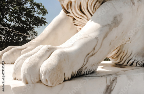 white sculpture close-up of marble paw of a lion on a pedestal in the sunlight