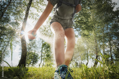 Hiker applying mosquito repellent on the leg skin in the forest.