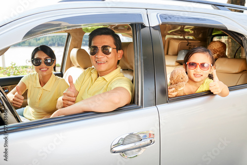 Portrait of Asian happy family in sunglasses sitting in their car showing thumbs up and they are going on summer holiday by car © Seventyfour