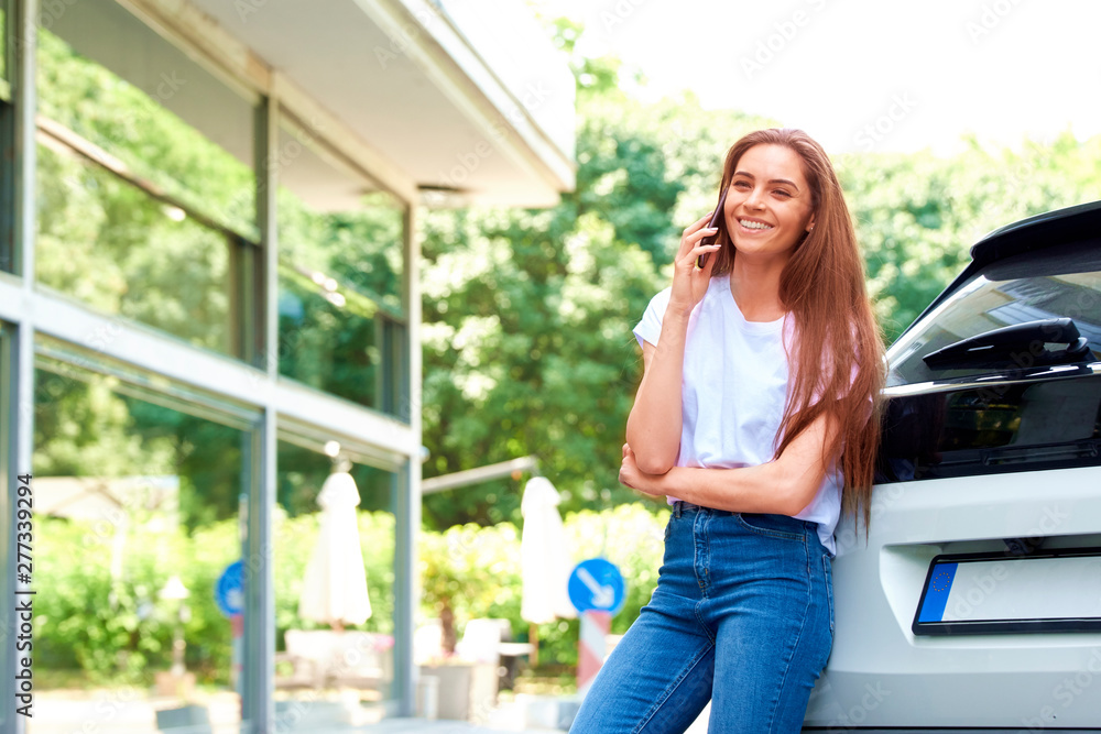 Young woman using her cell phone while standing on the street next to her car