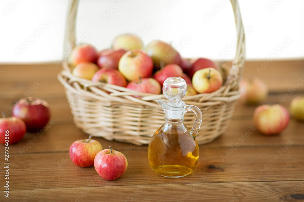 fruits, food and harvest concept - apples in wicker basket and glass jug of apple vinegar on wooden table fruits, food and harvest concept - apples in wicker basket and glass jug of apple vinegar on wooden table