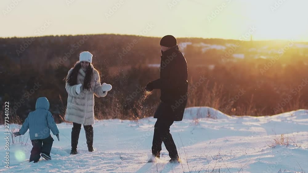 active family members in winter dressing play snowballs on snowy field against bright orange sunset slow motion