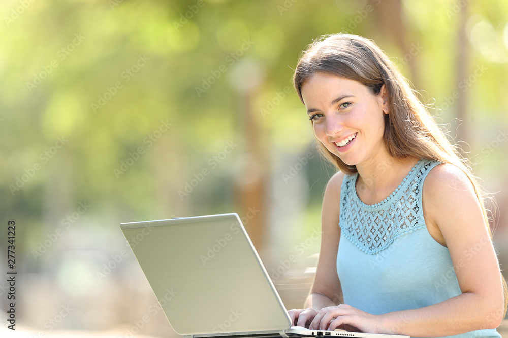 Happy woman with a laptop looks at camera in a park Happy woman with a laptop looks at camera in a park