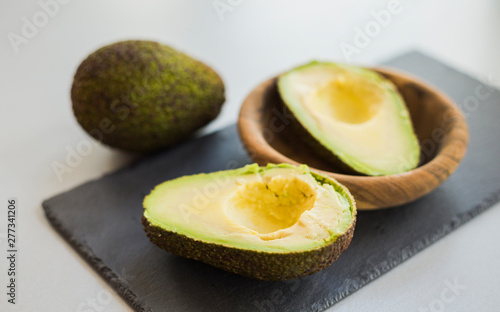 Sliced ripe green avocados in bowl on stone slate, close-up