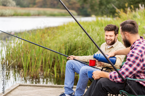 leisure and people concept - male friends fishing and drinking tea from thermos
