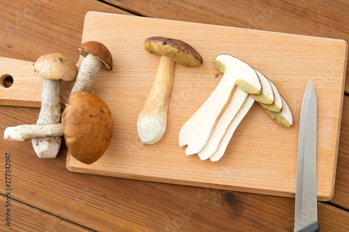 cooking, culinary and edible mushrooms concept - sliced brown cap boletus and kitchen knife on wooden cutting board photo