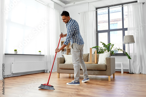 cleaning, housework and housekeeping concept - indian man with broom sweeping floor at home photo