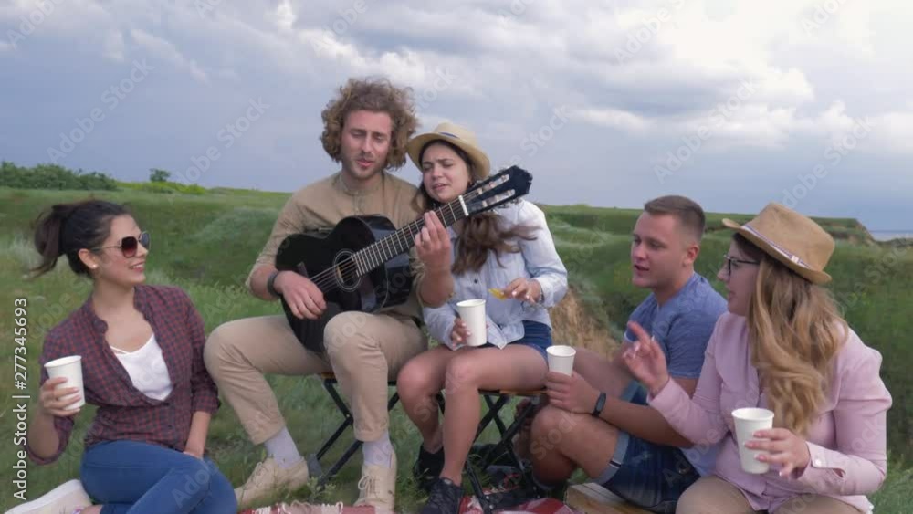 picnic, company of merry friends boys and girls play guitar and sing songs while nature recreation near river close-up picnic, company of merry friends boys and girls play guitar and sing songs while nature recreation near river close-up