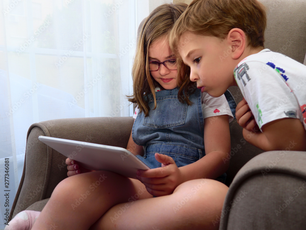 Brother and sister using digital tablet sitting on armchair in living room Brother and sister using digital tablet sitting on armchair in living room