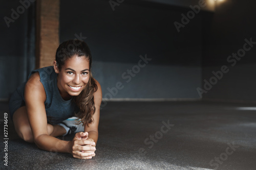 Attractive hispanic woman stretching body, sit with crossed leg, half-plank, doing fitness exercises, workout. Sportswoman warm-up before group training in gym, smile camera, motivated get fit