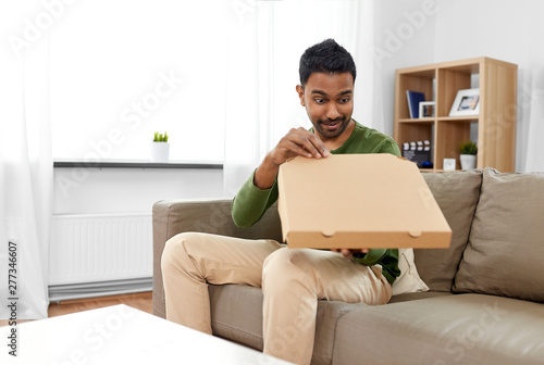 food delivery, consumption and people concept - excited indian man looking inside of takeaway pizza box at home