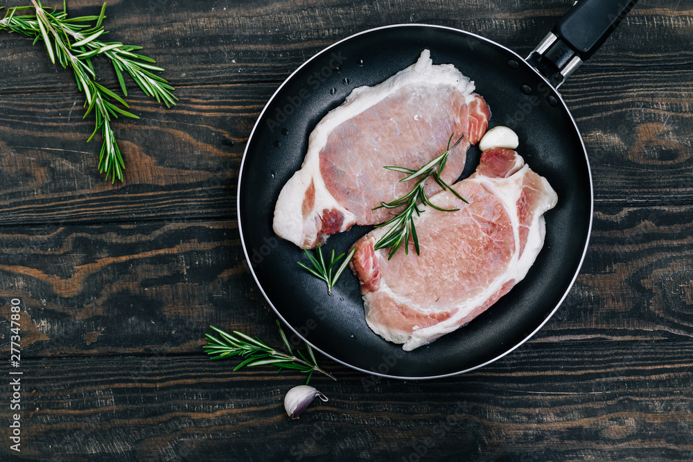 Raw pork steaks in a pan with rosemary and garlic