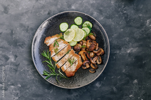 Dish of roasted meat, champignon mushrooms,cucumber and rosemary. Close up. Dark styled photo.