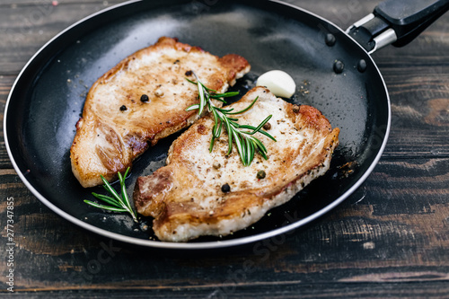 Roasted pork steaks in a frying pan with rosemary and garlic close up.
