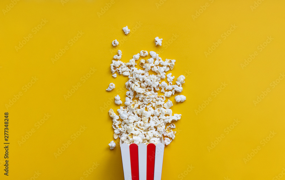 Popcorn in red and white cardboard box on the yellow back. Popcorn in red striped bucket on yellow background. Flat lay concept.