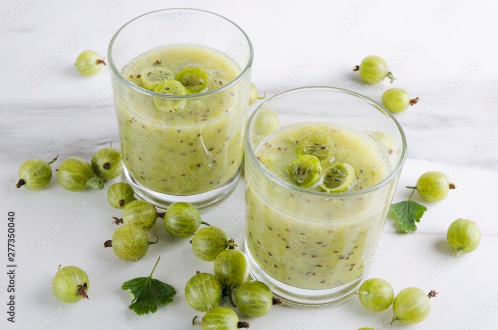 Closeup of two glasses of organic sweet smoothie, gooseberries on the white table Closeup of two glasses of organic sweet smoothie, gooseberries on the white table