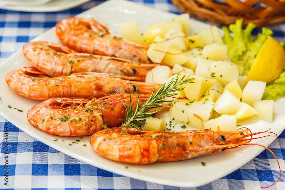 Large grilled shrimps with boiled potatoes on a white plate in a restaurant on the table.