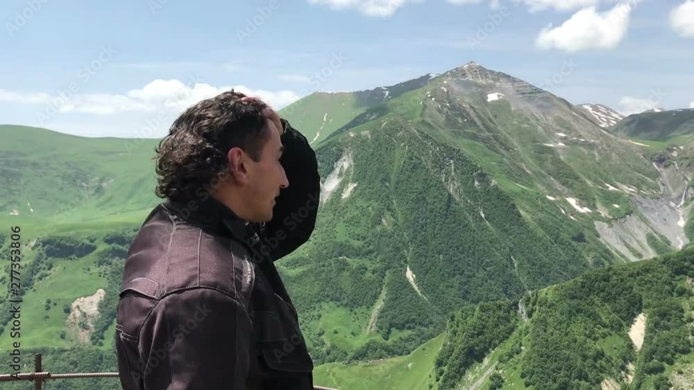 Man tourist putting of motorcycle helmet and looking around on point view in green caucasian mountains travel concept breath Man tourist putting of motorcycle helmet and looking around on point view in green caucasian mountains travel concept breath