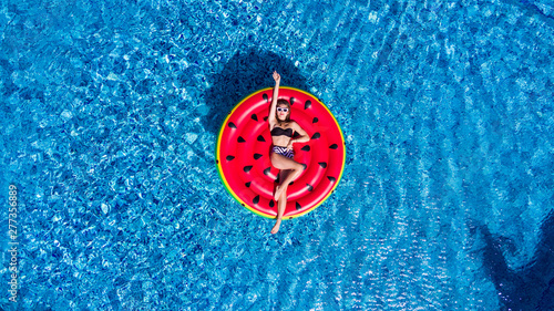 Top view of young woman relaxing on watermelon in pool. Young girl floating with fruit mattress. Summer holiday, luxury lifestyle and fashion concept