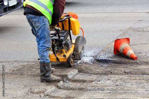 Worker cuts a piece of bad asphalt with a gasoline cutter during road construction.