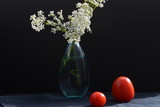bouquet of flowers in vase and tomatoes on black background