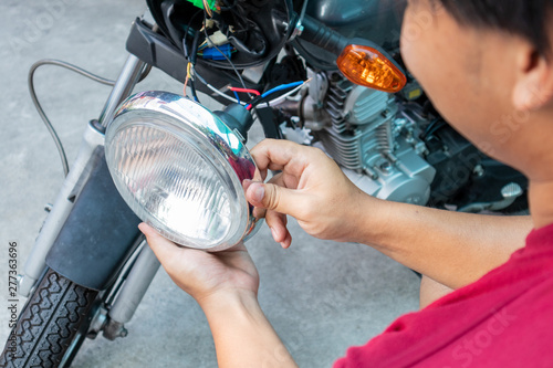 Asian young man fix or repair motorcycle lamp in garage. safety and check motorcycle. checking motorcycle before riding travel. Repair or maintanance concept. photo