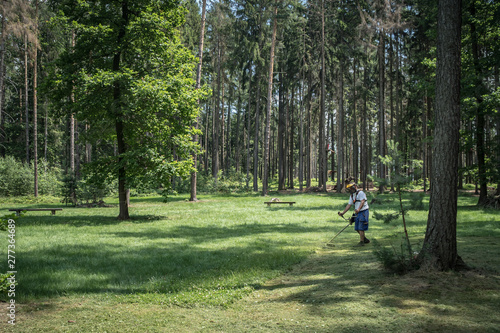 Mowing grasses in a meadow in the forest. Preparing for relaxation zone for rest in nature. Grill, sport, relax