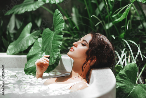 Fotografia Woman relaxing in round outdoor bath with tropical flowers, organic skin care, l