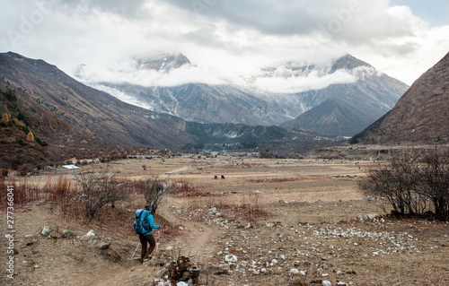 A woman trekker heading to Samagau valley on Manaslu circuit with view of Mount Manaslu range 8 156 meters. Himalayas, stone buildings in village, at Manaslu Glacier in Gorkha District in Nepal