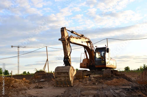 Large tracked excavator digs the ground for the foundation and construction of a new building in the city. Road repair, asphalt replacement, laying or replacement of underground sewer pipes - Image