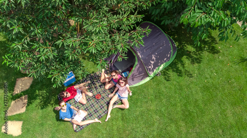 Aerial top view of family in campsite from above, parents and kids relax and have fun in park, tent and camping equipment under tree, family vacation in camp outdoors concept 