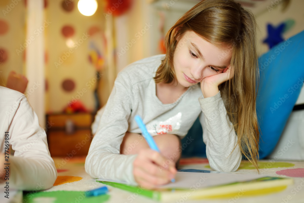 Two cute little sisters writing letters together at home. Older sister helping youngster with her homework. Two cute little sisters writing letters together at home. Older sister helping youngster with her homework.
