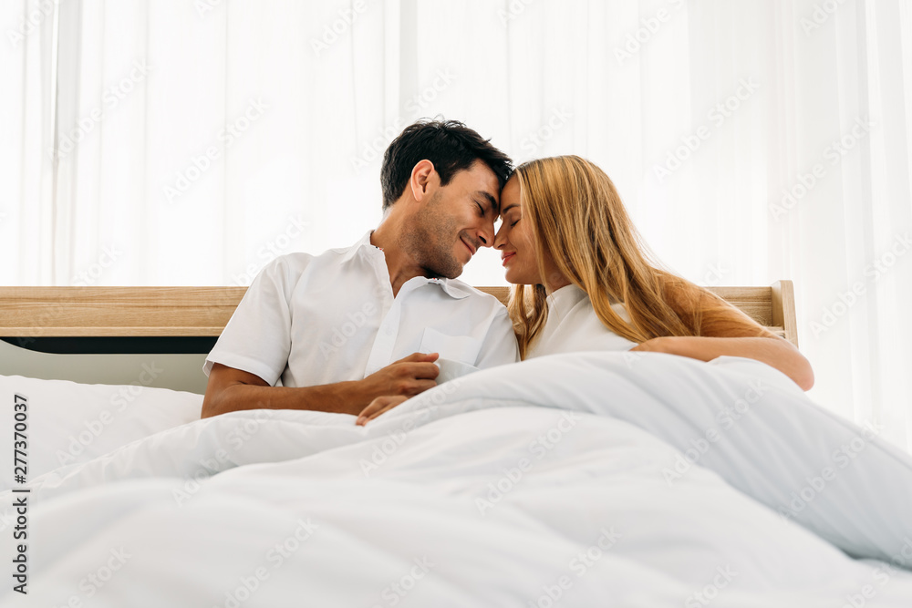 Fototapeta premium Couple lover wearing white smiling happy playing together on bed early morning
