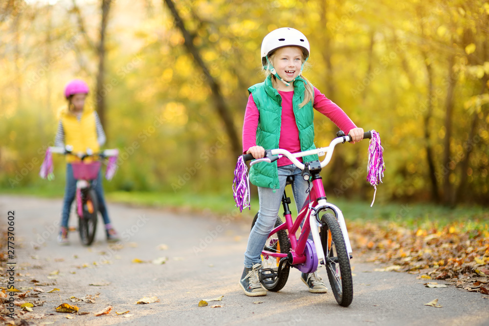 Cute little sisters riding bikes in a city park on sunny autumn day. Active family leisure with kids.