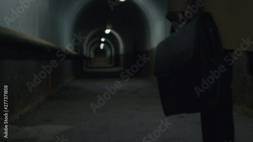 Low-section rear view shot of man in a coat with case walking through the tunnel in the evening photo