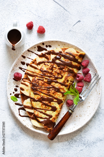 Crepe with chocolate paste, banana and raspberries on a concrete background. Tasty breakfast.