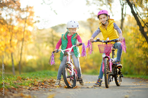 Cute little sisters riding bikes in a city park on sunny autumn day. Active family leisure with kids.